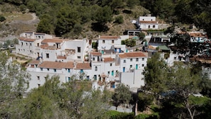 Uma vila costeira com edifícios brancos, telhados de terracota e vegetação densa.