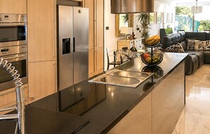 A modern kitchen with stainless steel appliances, a black countertop, and a dining area with a sofa and table. - 3 bedroom stunning home in Benalmádena (Benalmádena)