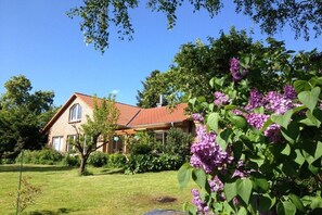 Ein Haus mit rotem Dach, umgeben von einer gepflegten Rasenfläche und blühenden Pflanzen.
