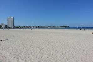 Ein weiter Sandstrand mit blauem Himmel, einem hohen Gebäude und einer kleinen Insel in der Ferne.