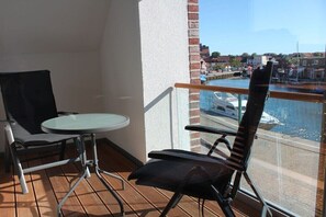 Ein Balkon mit Tisch und Stühlen, Blick auf einen Yachthafen mit Booten und eine Stadtkulisse im Hintergrund.