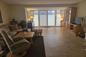 Ein Wohnzimmer mit Sofa, Couchtisch, Fernseher und einer Schiebetür zu einem Balkon.