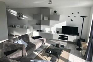 A modern living room with a grey sofa, a flat-screen TV, and built-in shelves. - Holiday home in Makkum with swimming pool (Makkum)