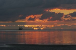 A sunset over a calm sea with a sailboat in the distance. - Holiday home in Makkum with swimming pool (Makkum)
