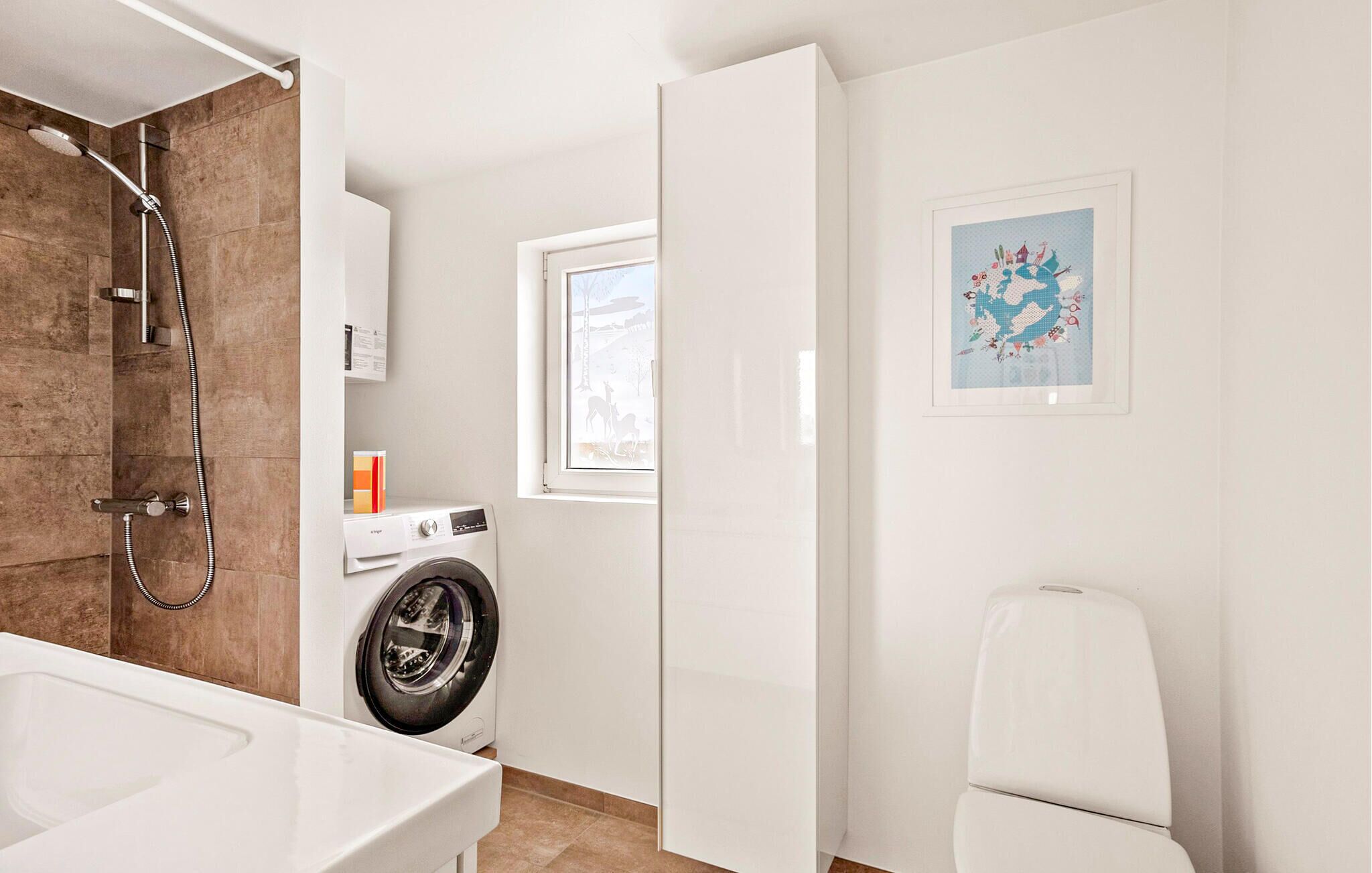 A modern bathroom with a shower, a washing machine, a toilet, and a window with a view.