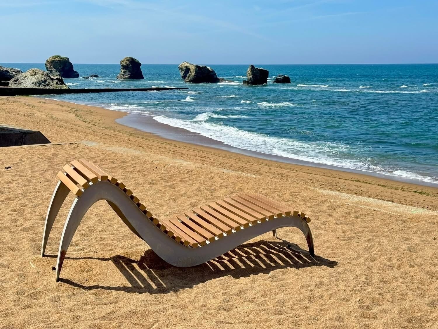 Una playa con una silla de madera y formaciones rocosas al fondo.
