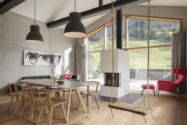 Ein modernes Interieur mit Essbereich, Kamin und großen Fenstern mit Blick auf eine Landschaft.