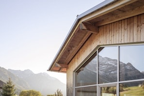 Ein Holzhaus mit großen Fenstern, einem geneigten Dach und einer Bergkulisse.