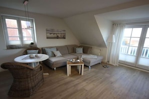 A cozy living room with a sofa, a small table, a wicker chair, and a window with curtains. - Holiday apartment with 2 bedrooms (Sankt Peter-Ording)