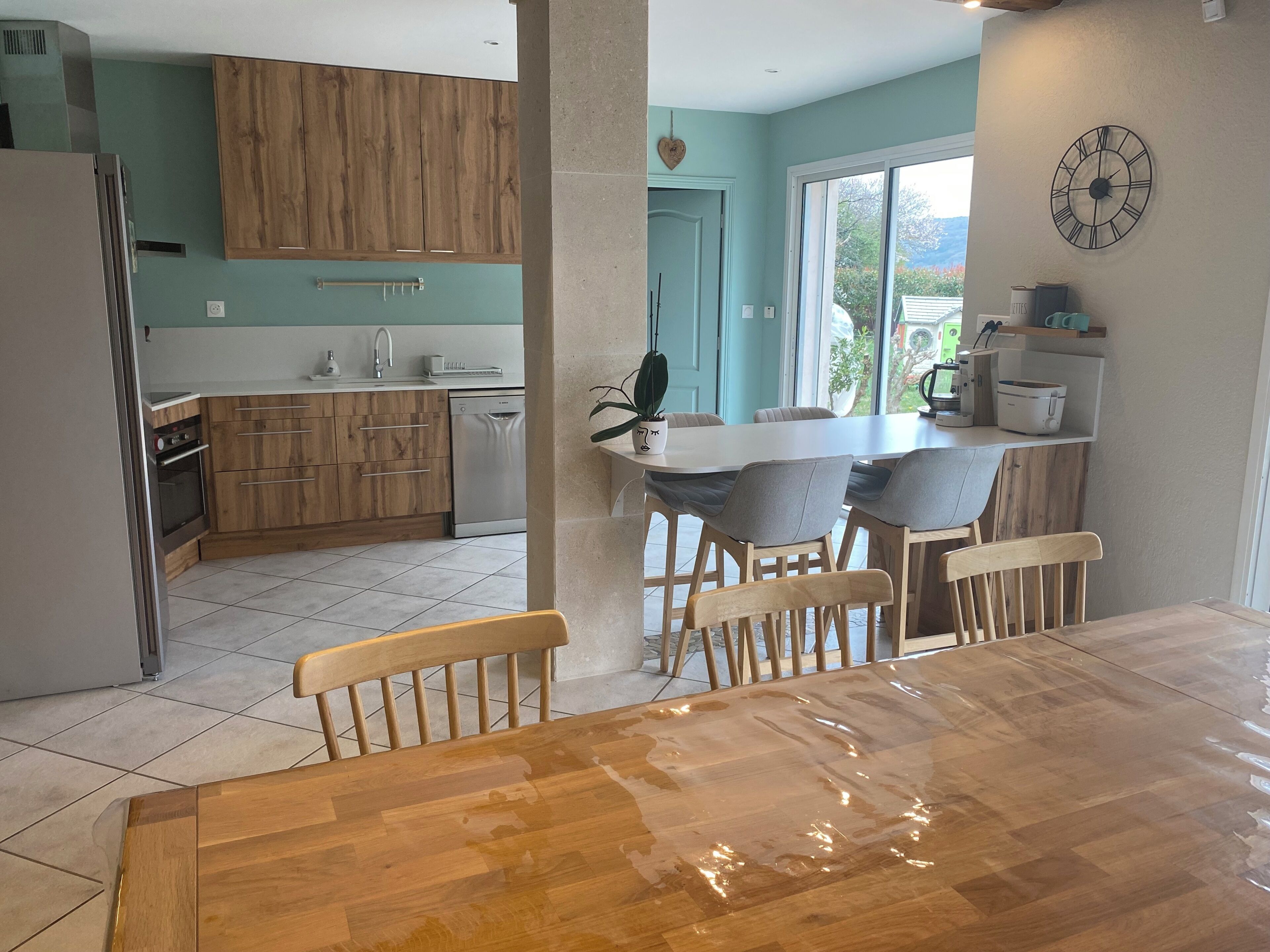 A modern kitchen with wooden cabinets, a stainless steel refrigerator, and a dining area with a wooden table and chairs.