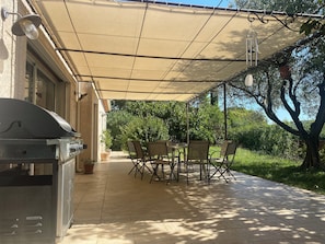 Eine Terrasse im Freien mit Grill, Esstisch, Stühlen und einem überdachten Bereich.