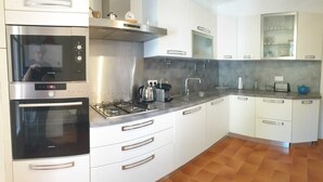Una cocina moderna con electrodomésticos de acero inoxidable, armarios blancos y piso de baldosas.