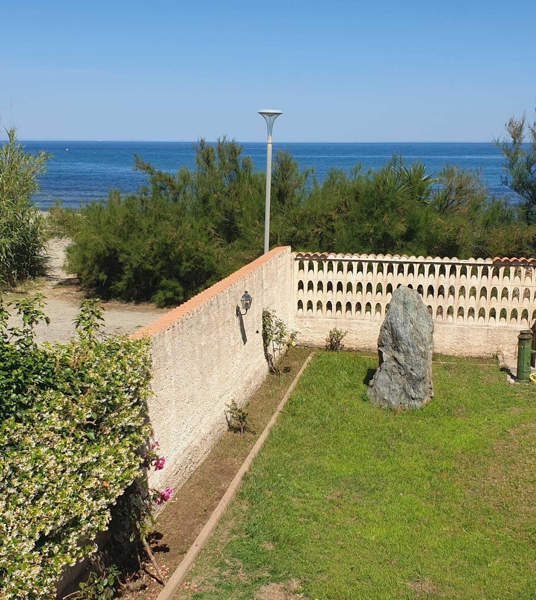 Un jardin situé sur la côte, avec un mur de pierres, un sentier et un grand rocher.