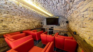 Ein Zimmer mit Steinwänden, einem an der Wand befestigten Flachbildfernseher, rot gepolsterten Sitzmöbeln und Holzboden.