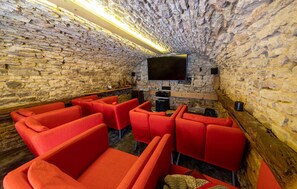 A stone-walled room with a flat-screen TV mounted on the wall, red upholstered seating, and a wooden floor. - Ancienne Maison de Vigneron (Chasselas)
