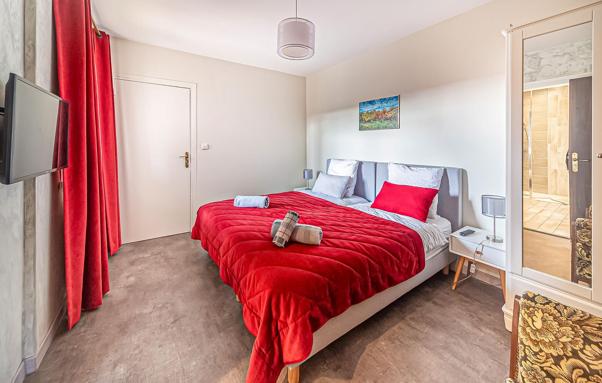 A bedroom with a bed, a television, a nightstand, a lamp, and a painting on the wall.