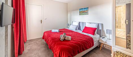 A bedroom with a bed, a television, a nightstand, a lamp, and a painting on the wall.