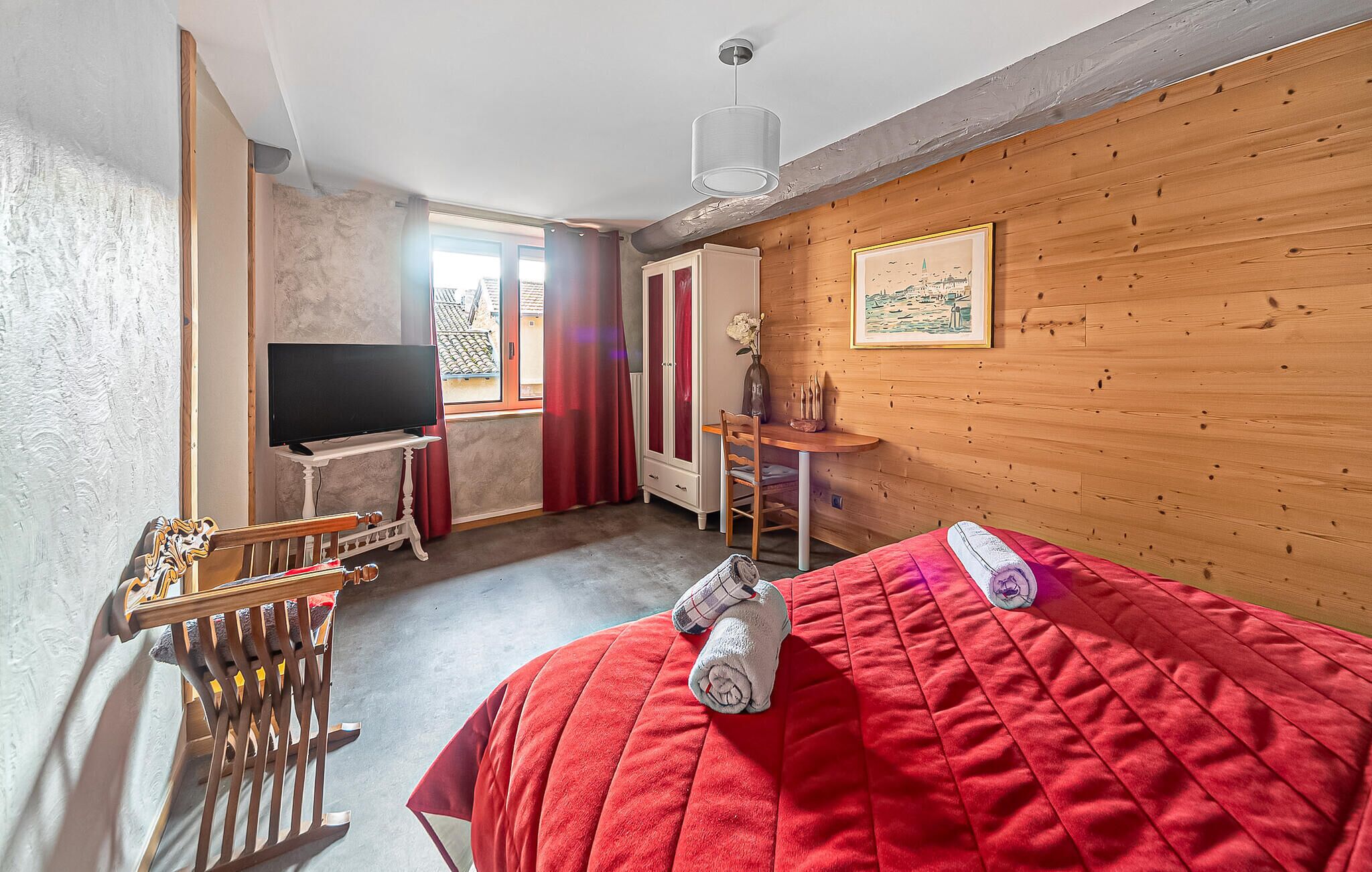 Een kamer met een bed, een televisie, een houten wand, een raam en een deur.