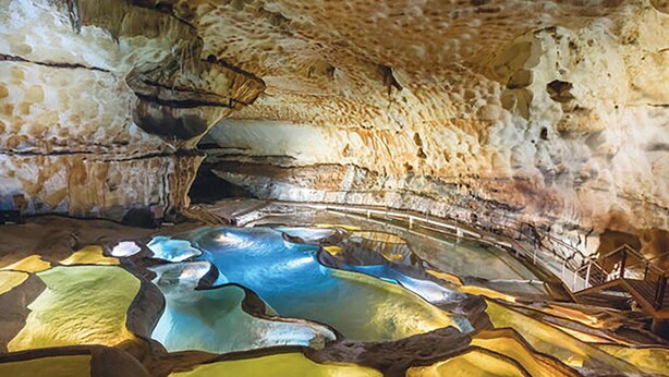 Interior de una cueva con estalactitas, un estanque de agua y una estructura de madera.