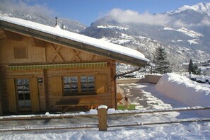 Eine Holzhütte mit schneebedecktem Dach, einer Holzterrasse und einem Bergpanorama.