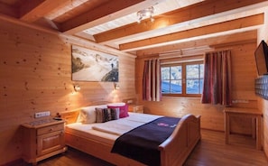 Ein Schlafzimmer einer Holzhütte mit einem Bett, Nachttischen, einem Fenster mit Vorhängen und einem Bild an der Wand.