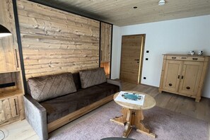 Ein Zimmer mit Holzwandverkleidung, einer Couch, einem kleinen runden Tisch und einer Holzkommode.