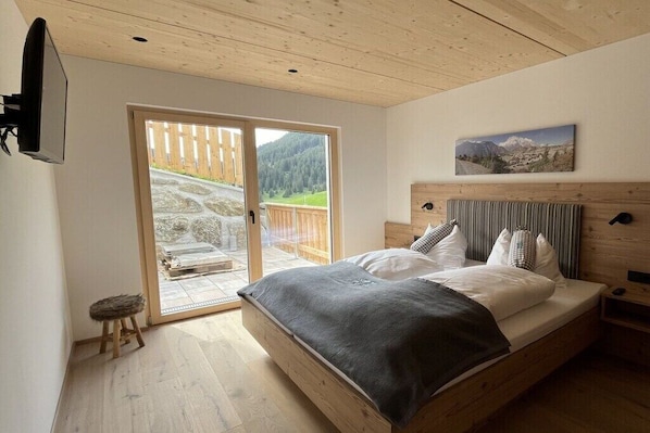 A bedroom with a wooden bed, a large sliding glass door to a balcony, and a painting on the wall. - Severin Quarter || Berwang (Berwang)