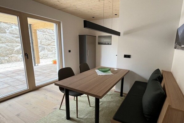 Ein modernes Interieur mit einem Holzesstisch, schwarzen Stühlen, einer grünen Schüssel, einem schwarzen Sofa und einer Steinwand.