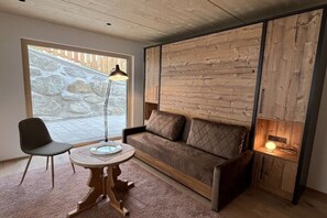 A cozy room with a stone wall, a wooden sofa, a round table, and a lamp. - Severin Quarter || Berwang (Berwang)