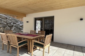 An outdoor wooden table with chairs, a stone wall, and a door.