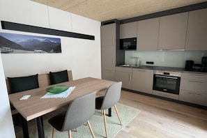 A modern kitchen with a built-in oven, a dining area with a wooden table and chairs, and a kitchen island.