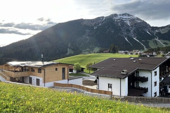 A mountain village with modern buildings, a ski slope, and a large mountain in the background.