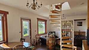 A spacious living area with a wooden spiral staircase, a dining table with chairs, and a large barrel. - Cosy Cottage close to Munros and cycle route (Lochearnhead)