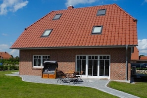 Ein zweistöckiges Haus mit rotem Ziegeldach, einer Ziegeläußeren und einer Terrasse mit Gartenmöbeln.