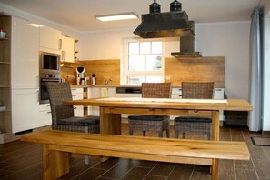 Eine kleine Küche mit weißen Schränken, einem Holztisch, Korbstühlen und einer Bank.
