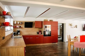 A modern kitchen with red cabinets, a wooden countertop, and a dining area with a red tablecloth. - Holiday home in Hayingen with barbecue (Hayingen)
