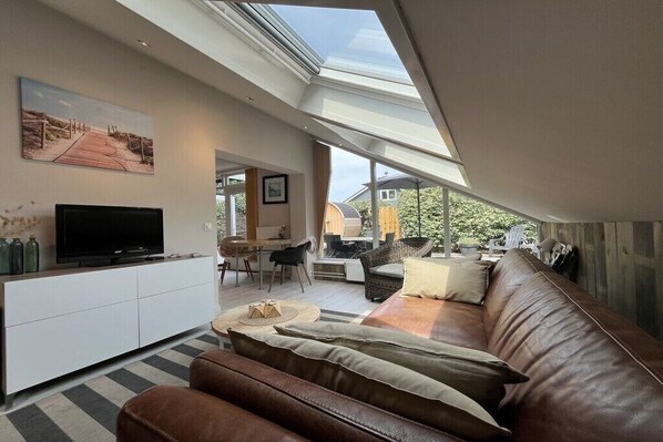 A modern living room with a TV, sofa, and dining area. - Holiday home with 1 bedroom (Callantsoog)
