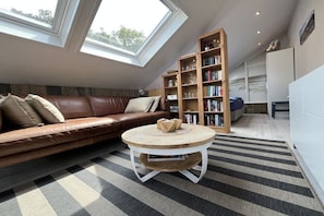 A modern living room with a leather sofa, a round coffee table, a bookshelf, and skylights. - Holiday home with 1 bedroom (Callantsoog)
