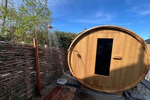 A wooden sauna with a door, a showerhead, and a bamboo fence. - Holiday home with 1 bedroom (Callantsoog)