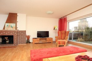 Ein Wohnzimmer mit Kamin, Fernseher, einem roten Sofa, einem Holztisch und einem großen Fenster mit Blick.