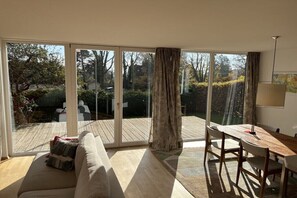 A room with a sliding glass door leading to a deck, a wooden table, and a sofa. - Holiday home with 2 bedrooms (Herrsching)