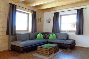 A cozy living room with a sectional sofa, two windows with curtains, a small table, and a wall-mounted light fixture.