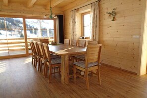 A wooden dining table with chairs, large windows with curtains, and a view of snow-covered mountains.