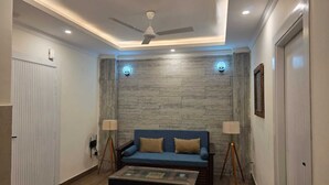 A living room with a sofa, two lamps, a ceiling fan, and a wooden wall. - The Bunny House Homestay (Mussoorie)