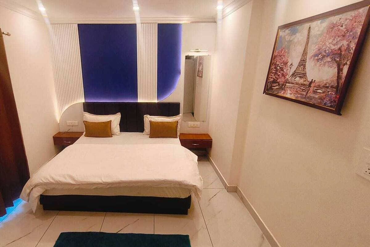 Un dormitori amb llit, taulells de nit, un quadre i una finestra amb cortines.