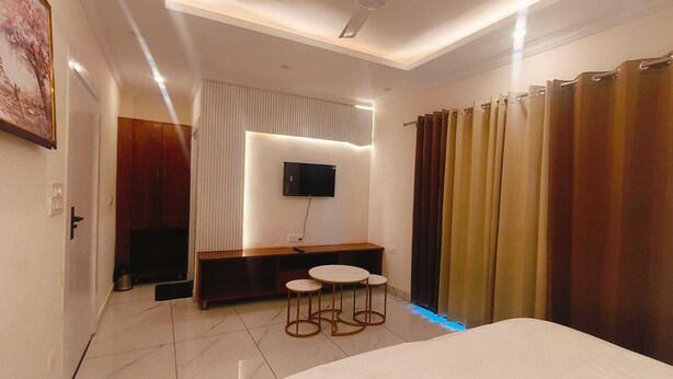 A modern hotel room with a bed, a TV mounted on the wall, a small seating area with stools, and a curtain on the window. - The Bunny House Homestay (Mussoorie)
