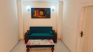 A room with a teal sofa, a floral-patterned ottoman, and a wall-mounted painting. - The Bunny House Homestay (Mussoorie)