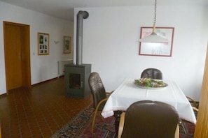 Ein Essbereich mit Tisch, Stühlen, einem Teppich, einem Kaminofen und einer Hängelampe.