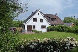 Ein weißes, zweistöckiges Haus mit geneigtem Dach, einer Veranda und einem gepflegten Rasen.