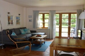 Ein Wohnzimmer mit einer Couch, einem Esstisch, einem Stuhl und einem Fenster mit Vorhängen.